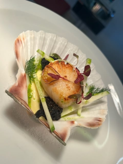 A scallop course served in a shell with cucumber and herbs